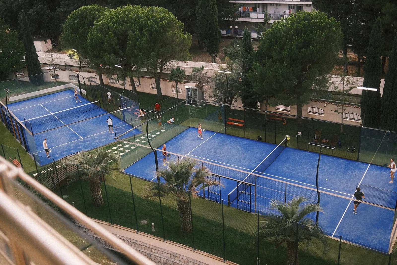 Beberapa lapangan padel biru dari atas dengan pemain yang sedang bertanding